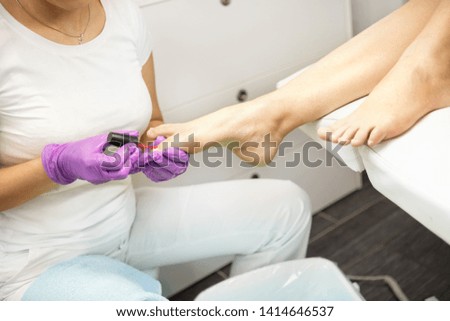Nail technician applying fingernail polish to woman's  nails on feet in nail salon