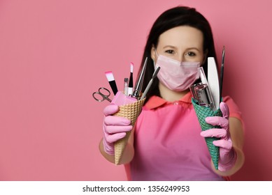 Nail technician in pink apron and gloves keeps at arms length instruments for nails salon in waffle cones brush, scissors, nail file with abrasive - Powered by Shutterstock