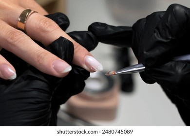 A nail technician wearing black gloves carefully applies a layer of gel polish to a client's fingernails. The close-up shot highlights the precision and professionalism in nail care. - Powered by Shutterstock