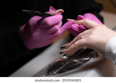 A nail technician wearing pink gloves carefully working on a client s nails - Powered by Shutterstock