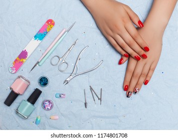 Nail work flat lay concept  Stylish trendy female manicure top view hands and red manicure   professional master tools: varnishes  nail file  scissors  frieze  sequins   pebbles