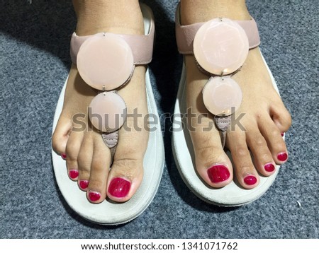 Nails art. Feet with hot pink pedicure. Bare feet with pedicure and wearing pink slippers over grey background. Pedicure on women's legs covered with pink varnish. Summer Holidays Vacation.