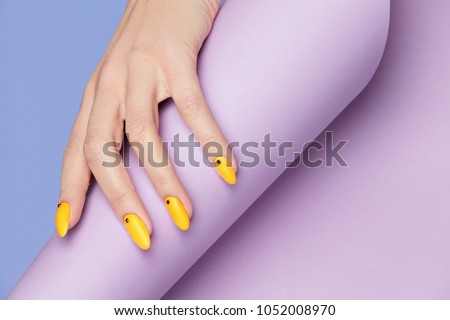 Nails Design. Hands With Bright Yellow Manicure On Violet Background. Close Up Of Female Hands With Trendy Orange Nails On Purple Background. Art Nail. High Quality Image.