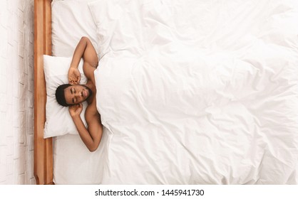 Naked african-american guy sleeping in bed with hands behind head, top view, free space