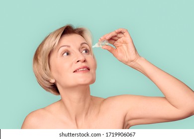 Naked Beautiful Blonde Mature Woman Standing Isolated On Blue Background Holding Healing Eye Drops Dropping Into Eyes Concentrated