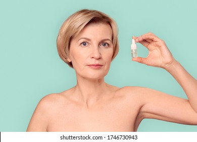 Naked Beautiful Blonde Mature Woman Standing Isolated On Blue Background Holding Healing Eye Drops Looking Camera Pensive