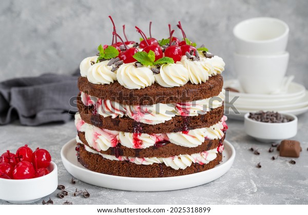 Naked Black forest cake, Schwarzwald pie. Cake with
dark chocolate, whipped cream and cherry on a gray concrete
background. Copy space