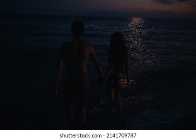 Naked Couple In Love Romantically Go Swimming At Night In Sea By Beach In Summer Under Moonlight. Atmospheric Lifestyle Photography With Soft Focus And Film Grain