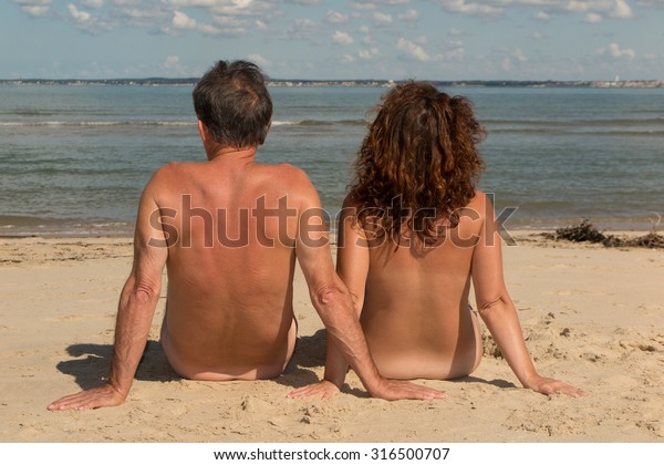 Naked couple sitting on the beach.