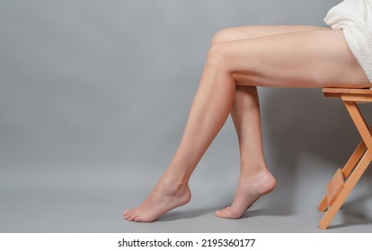 Naked Long Female Legs Sitting On Chair. Foot Massage. Gray Background. Side View.