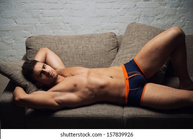 Naked male model lying on sofa on white wall background