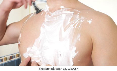 The naked man shaves his chest. A man with white foam for shaving on his chest. Men's shave body with foam and razor