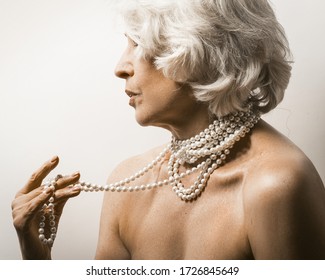 Naked mature woman on white. Profile view of a mature woman showing pearl beads on her neck and bare shoulders on white background. Beauty concept. Jewelry concept.