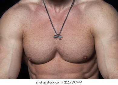 Naked Torso Of A Male Athlete In Close Up. The Body Of A Shirtless Bodybuilder With A Pendant In The Form Of A Silver Dumbbell. Jewelry Barbell. The Muscular Chest Of A Man In Love With Sports.