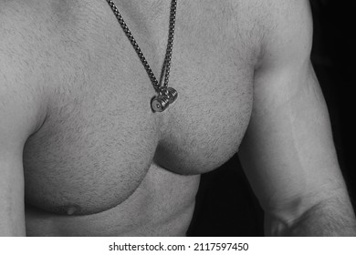 Naked Torso Of A Male Athlete In Close Up. The Body Of A Shirtless Bodybuilder With A Pendant In The Form Of A Silver Dumbbell. Jewelry Barbell. The Muscular Chest Of A Man In Love With Sports.