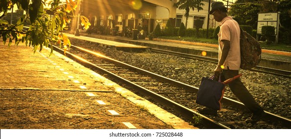 Nakhon Ratchasima, Thailand - August18, 2017: A man carrying luggage across a railroad track with warm sunshine - He is about to board a train to leave his home.  - Cinematic Style