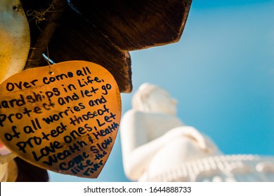 Nakkerd Hill, Phuket/Thailand-15December2019: Golden heart shaped praying bells hanging together in a row with people spiritual notes written on them and big buddha in the background