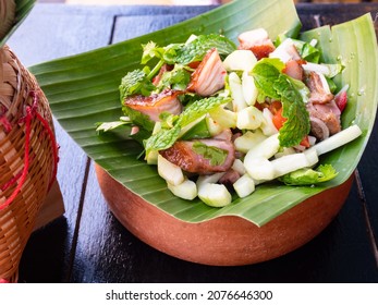 Nam Tok Moo, traditionelles thailändisches Essen mit gegrillter Schweinekleite, Kalksaft, Minzblätter, Gurken, Knoblauch und Chilischoten auf Palmenblättern.