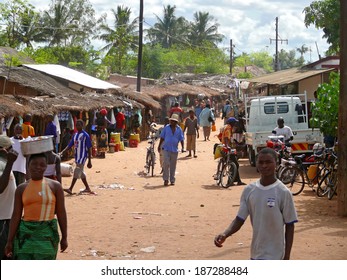 NAMAPA, MOZAMBIQUE - 6 DECEMBER 2008: Strangers Villagers Go About Their Business In Namapa, Mozambique - 6 December 2008. Residential Buildings With Thatched Roofs Around. Transport  On The Road. 