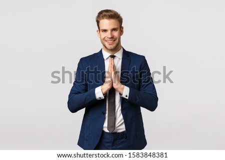 Namaste. Handsome young caucasian businessman greeting asian business partners, hold hands together in pray, supplicating or greeting gesture, smiling friendly, standing white background