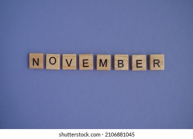The name of the month of November is written on wooden cubes isolated. Very Peri Color of the Year 2022 background, copy space. Top view of wooden blocks with letters. Step by step, step 11.