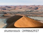 Namibia landscape with sand hills and dunes in Sossusvlei, Namib-Naukluft National Park, Namibia. Panorama of Namib desert with tourists walking up to red sand dunes at sunrise.