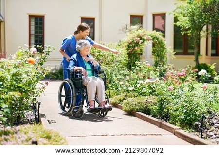 Naming the flowers as they go. Shot of a resident and a nurse outside in the retirement home garden.