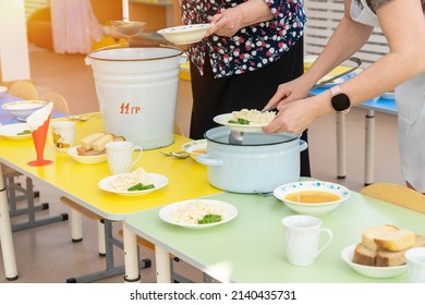 Nannies In Kindergarten Put Food On Plates And Serve Tables Before Lunch