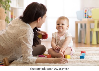 Nanny or babysitter looks after kid toddler. Baby girl playing with educational toys in nursery. Child having fun with colorful different toys at home.