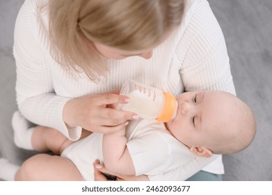 Nanny carefully holds infarct in her arms, baby drinks formula from bottle held by woman, close-up. Concept of healthy eating, artificial nutrition, infant feeding, professional nanny