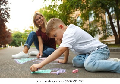 Nanny with cute little boy drawing house with chalks on asphalt