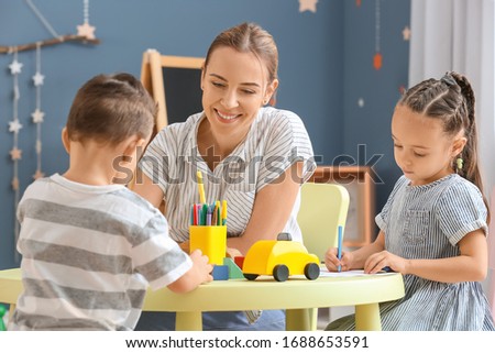 Nanny with cute little children playing and drawing at home