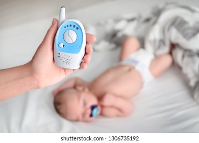 Nanny Holding Baby Monitor And Sleeping Child On Background