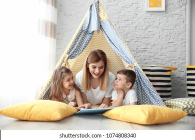 Nanny And Little Children Reading Book In Tent At Home