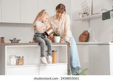 Nanny with little girl watering plant on table in kitchen - Powered by Shutterstock