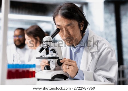 Nanotechnology researcher using microscope to evaluate cellular structures in lab. Research facility expert observes medical tissue through magnification tool at laboratory bench workstation