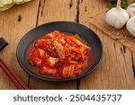 Napa cabbage kimchi topped with white sesame seed in black plate,Korean fermented side dish food.