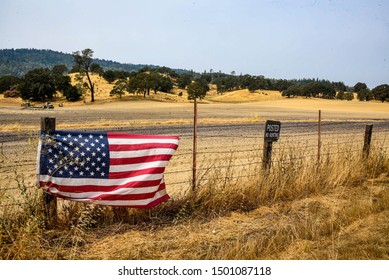 Napa, California / USA-8/21/18: American Flag On A Barb Wire Fence Surrounding Farming Open Land With A Sign Post Saying 