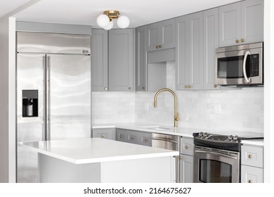 NAPERVILLE, IL, USA - MARCH 3, 2022: A Grey Kitchen With Stainless Steel Appliances, Gold Faucet, White Marble Countertops, And A Subway Tile Backsplash.