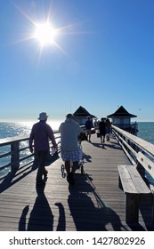 Naples, FL/USA: Feb 28, 2019 - Visitors With Fishing Equipment Walk On Classic Landmark The Pier, Popular For Exquisite Sunsets And Boatless Fishing, As Blazing Sun Begins To Set In Cloudless Blue Sky