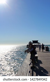 Naples, FL/USA: Feb 28, 2019 - Visitors With Fishing Equipment Stand On Landmark The Pier, Popular For Exquisite Sunsets And Boatless Fishing, As Blazing Sun Begins To Set In The Cloudless Blue Sky. 