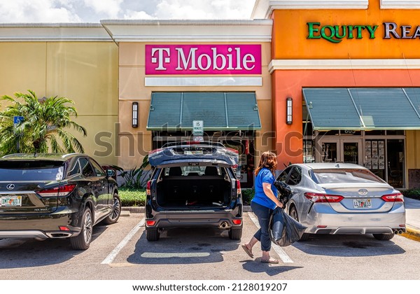 Naples, USA - August 7, 2021: Naples,\
Florida T-Mobile office and parking lot candid people and Equity\
Realty real estate sign for business in strip\
mall