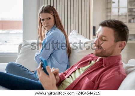 Narcissist, egoist, uncaring man scrolling social networks, messaging in smartphone with joyful face expression, neglecting woman. Offended upset wife with reproachful glance thinks of divorce