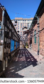 A narrow alley enclosed by metal lights and a wooden and a brick wall
