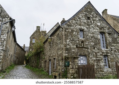 A narrow alley in Locronan, lined with stone houses. The wet cobblestones reflect the grey autumn sky, giving the scene a calm and intimate atmosphere. - Powered by Shutterstock