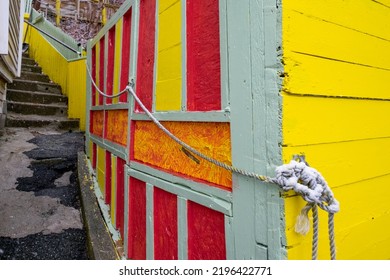 A Narrow Alleyway Leading Upward To Houses With Concrete Steps, Colorful Red, Yellow And Green Walls, An Old Rope As A Railing Affixed To A Wooden Wall. There Are House Windows And External Walls. 