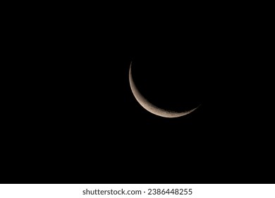 A narrow crescent of the waning moon in the night sky.