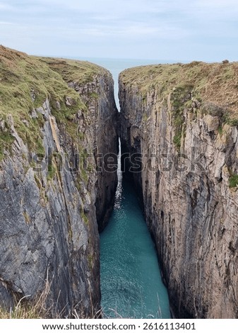Narrow gap between 2 cliffs with blue sea between - Huntsman's Leap, Pembrokeshire, Wales