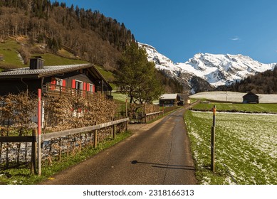 Narrow road with houses and view to the snow-covered Mt. Saentis, Wildhaus-Alt St. Johann, Toggenburg, Canton St. Gallen, Switzerland