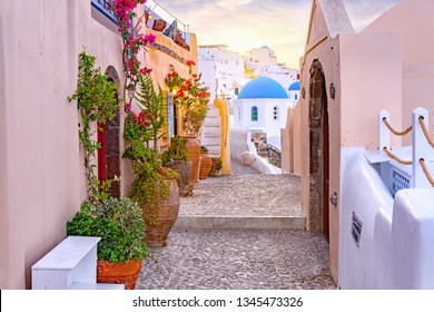Narrow scenic street of Oia Village on Santorini Island at sunset, Greece.